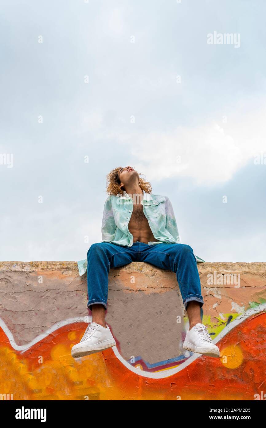 Young blond man sittung on a wall and looking up Stock Photo