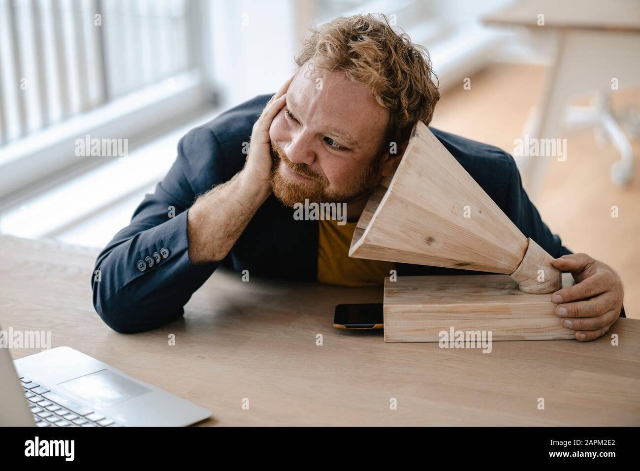 Businessman leaning on desk in office listening to music with a wooden gramophone Stock Photo