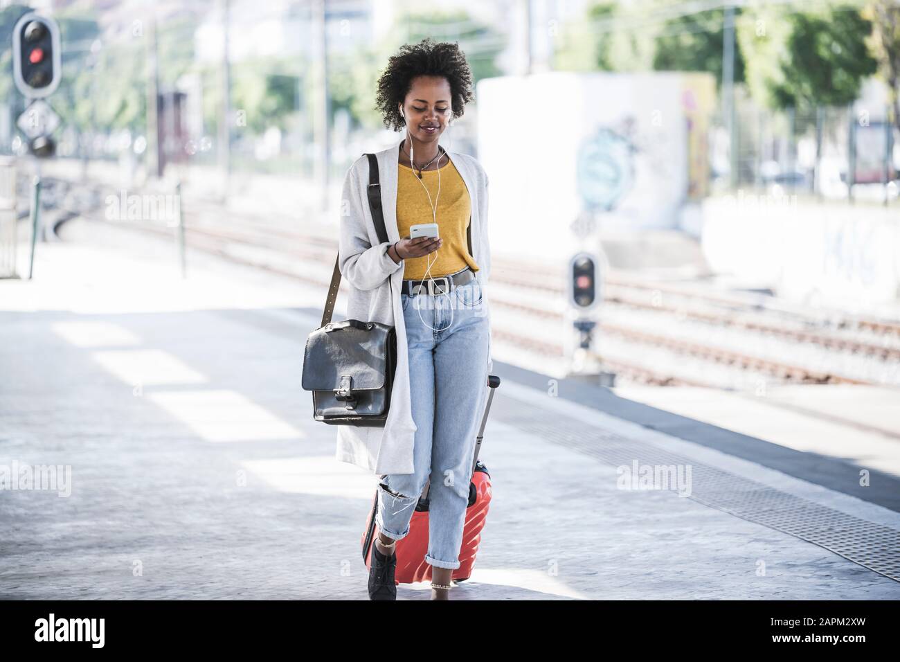 Smiling young woman with cell phone and earphones at the train station Stock Photo