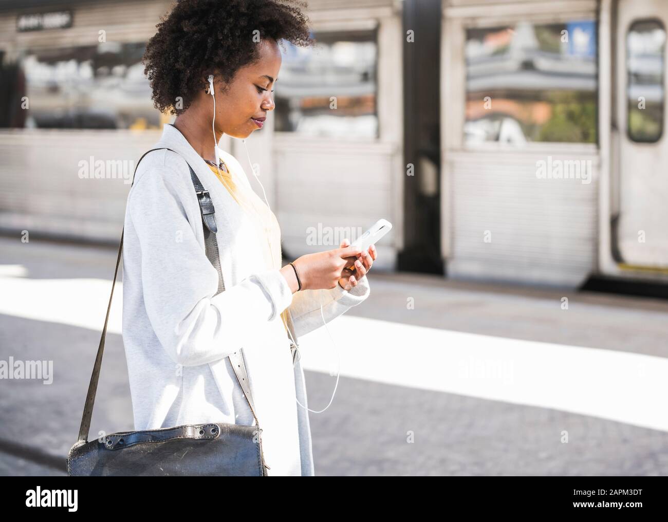 Young woman with cell phone and earphones at the train station Stock Photo