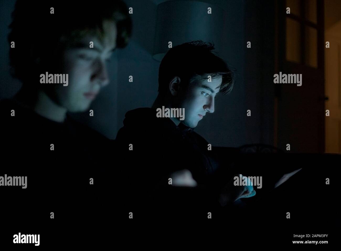 Two teenage boys using technology at home in the dark Stock Photo