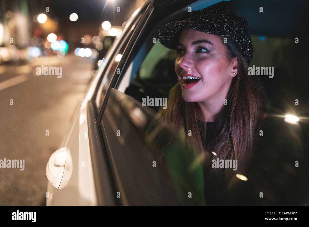 Woman sitting on the backseat of a car in the city at night, looking out of the car window Stock Photo