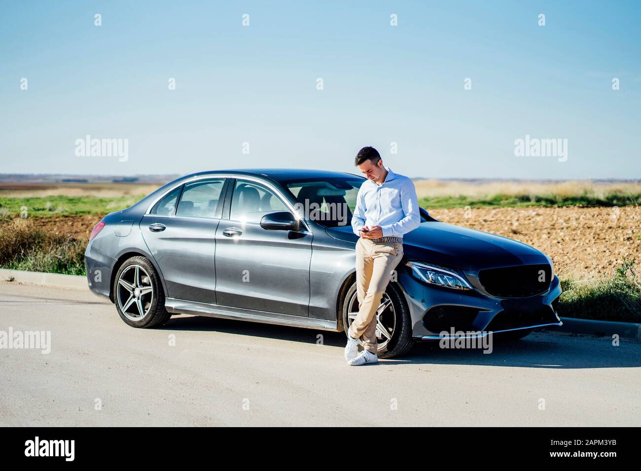 Young businessman leaning against car on country road using smartphone Stock Photo