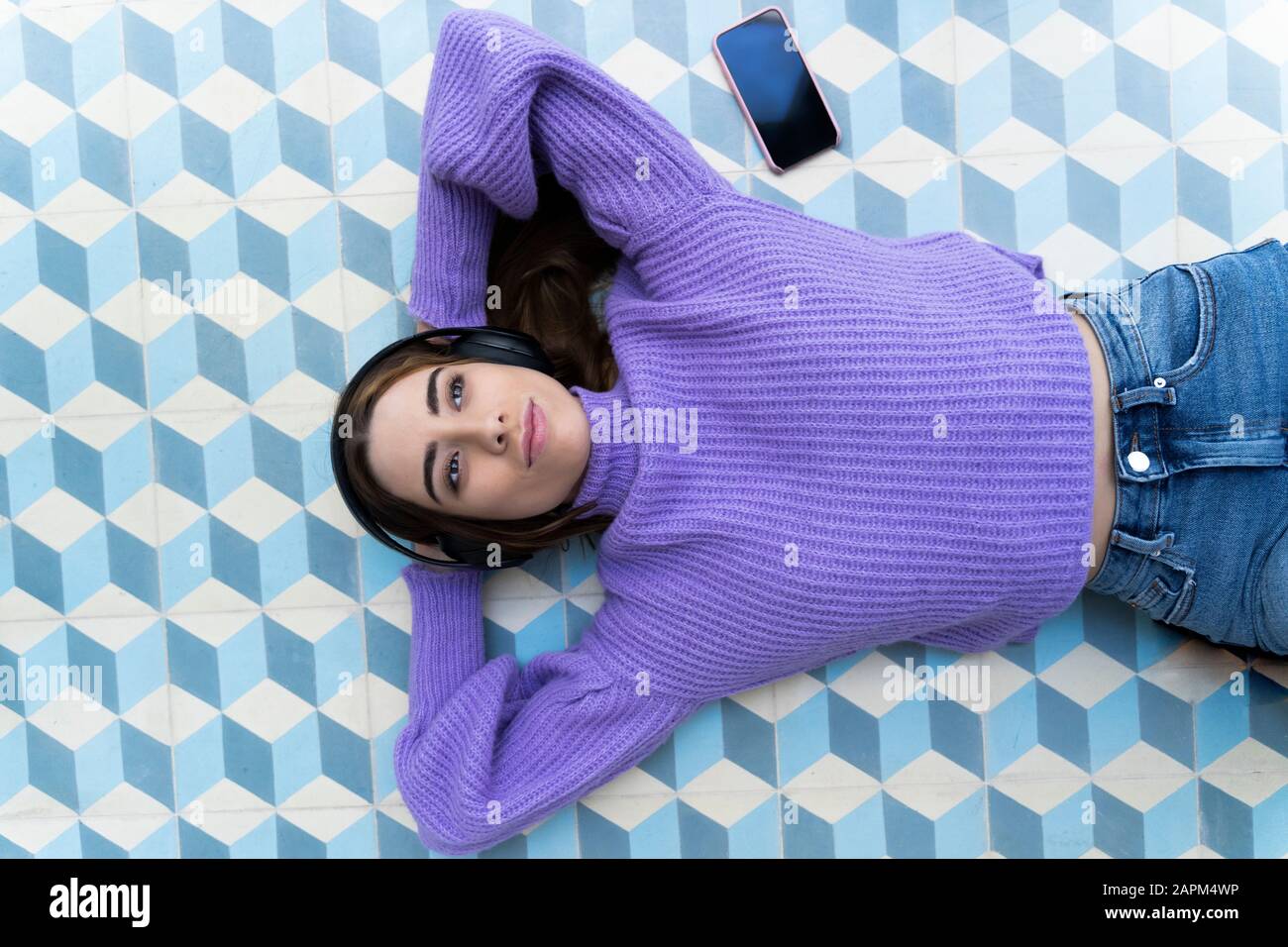 Portrait of happy young woman lying on the floor listening music with ...