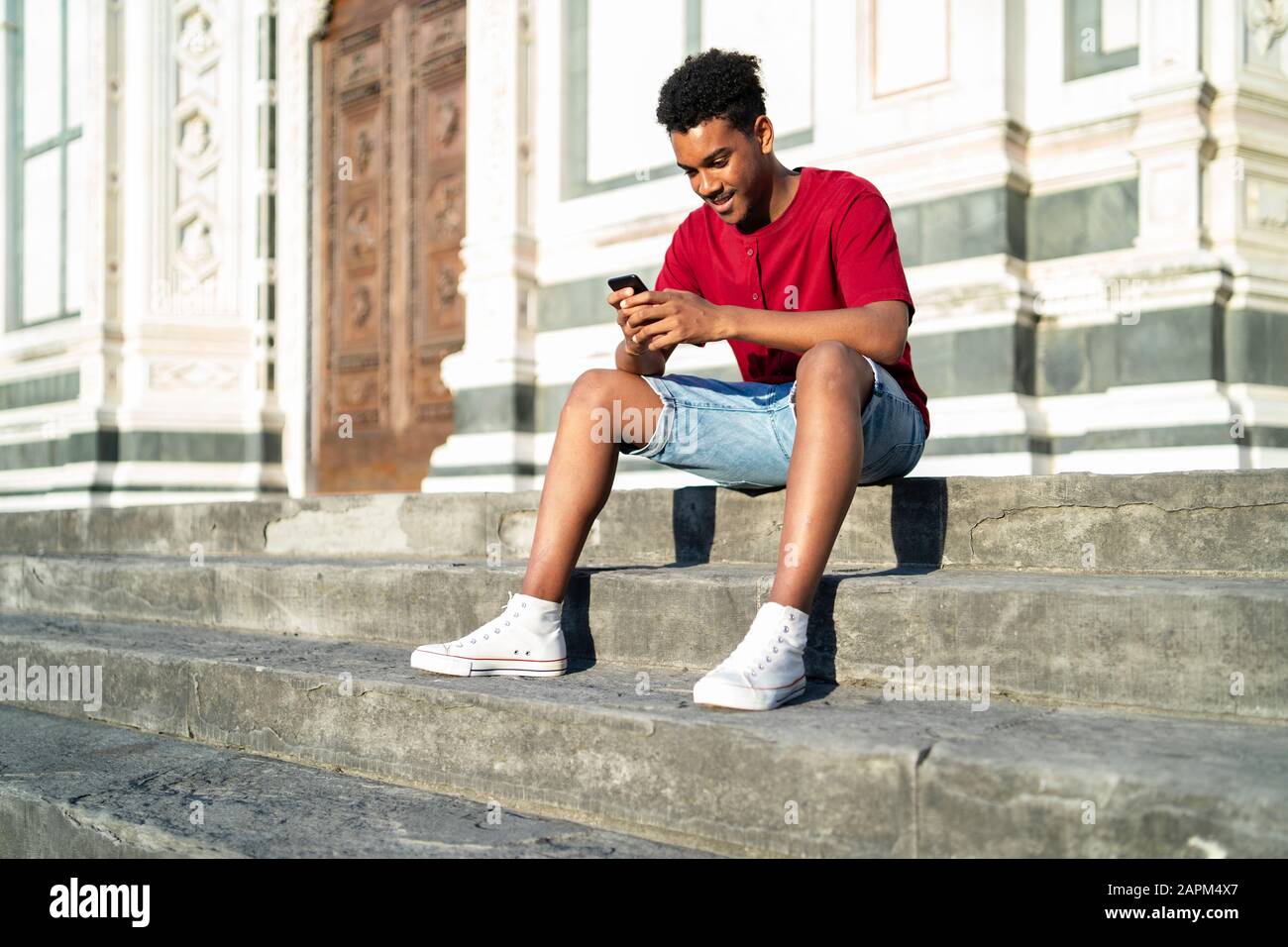 Young man sitting on outdoor stairs checking his smartphone, Florence ...