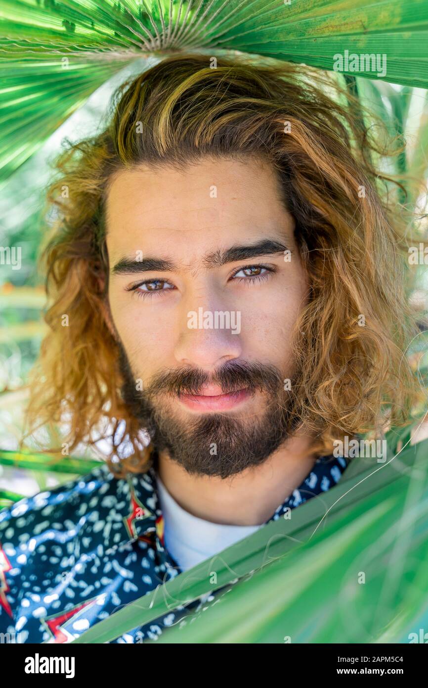 Portrait of bearded young man with dyed hair among palm leaves Stock Photo