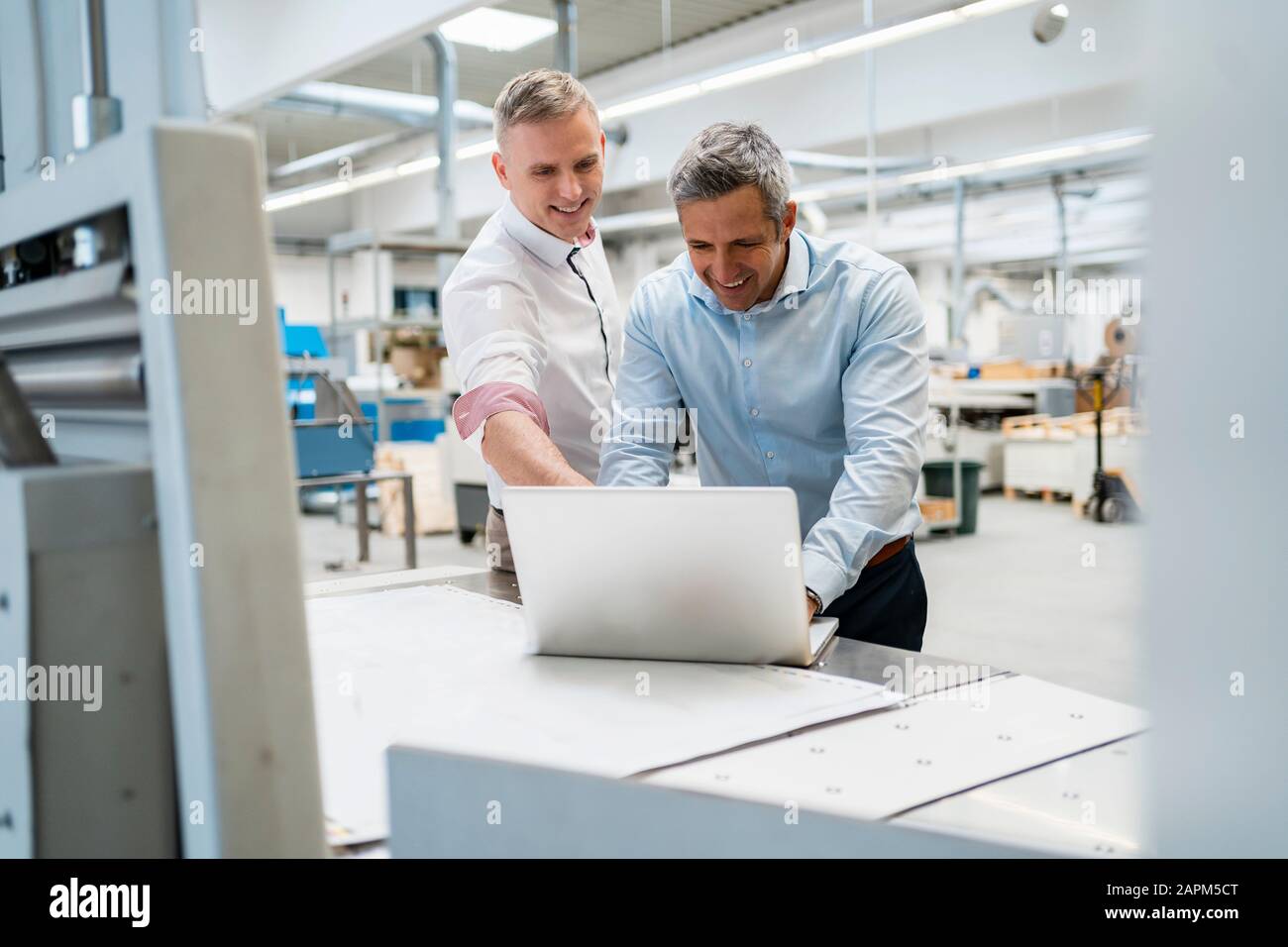 Two smiling colleagues using laptop in a factory Stock Photo