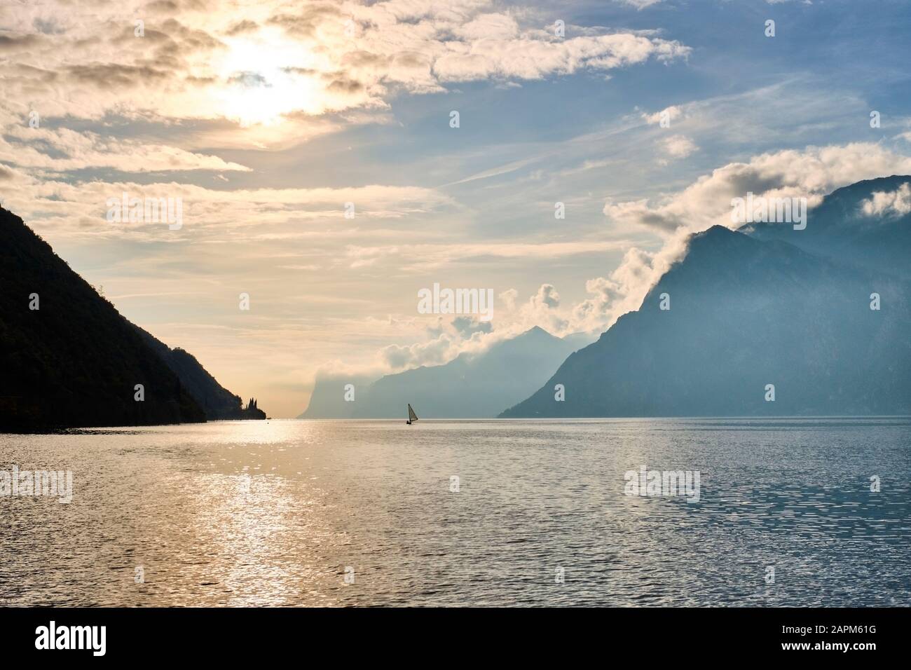 Italy, Trentino, Nago-Torbole, Silhouette of sailboat sailing near coastal cliffs of Lake Garda at moody sunrise Stock Photo