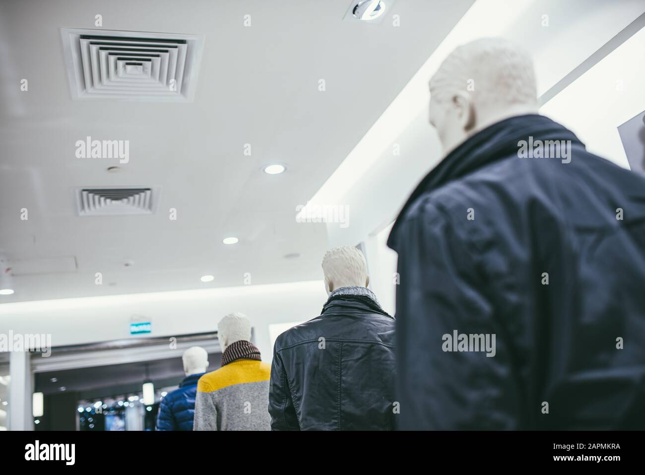 mannequins stand in a row in the store and are dressed in different clothes. Bottom-up view of the ceiling. Stock Photo