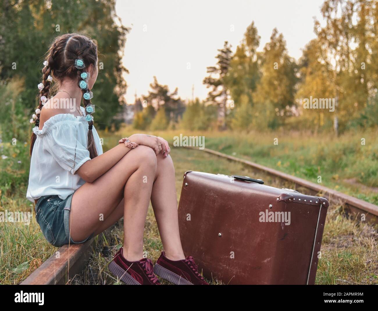 A teenage girl is sitting with a suitcase on the railway tracks Stock