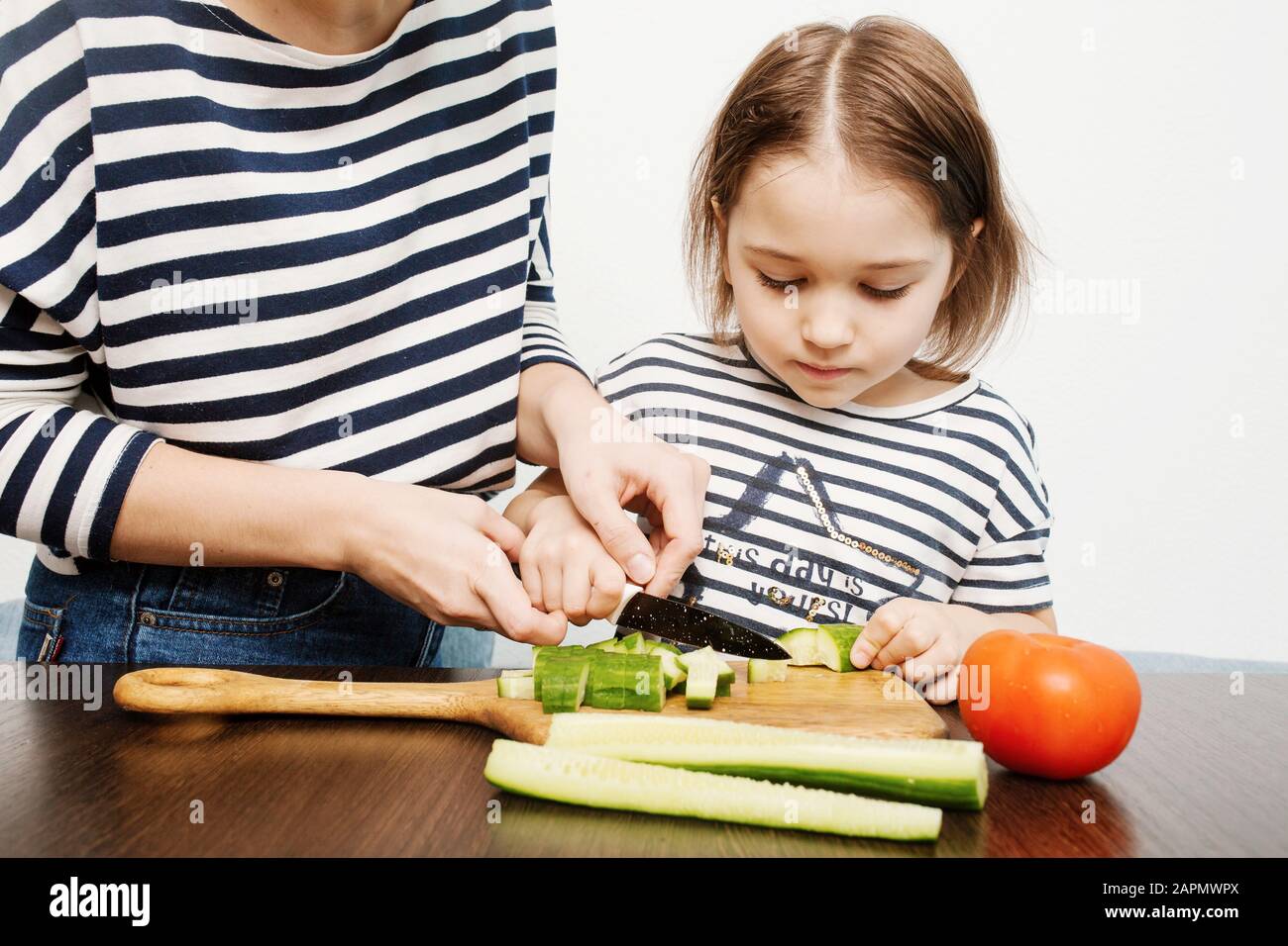 Young mother teaches her little daughter to cut vegetables for healthy