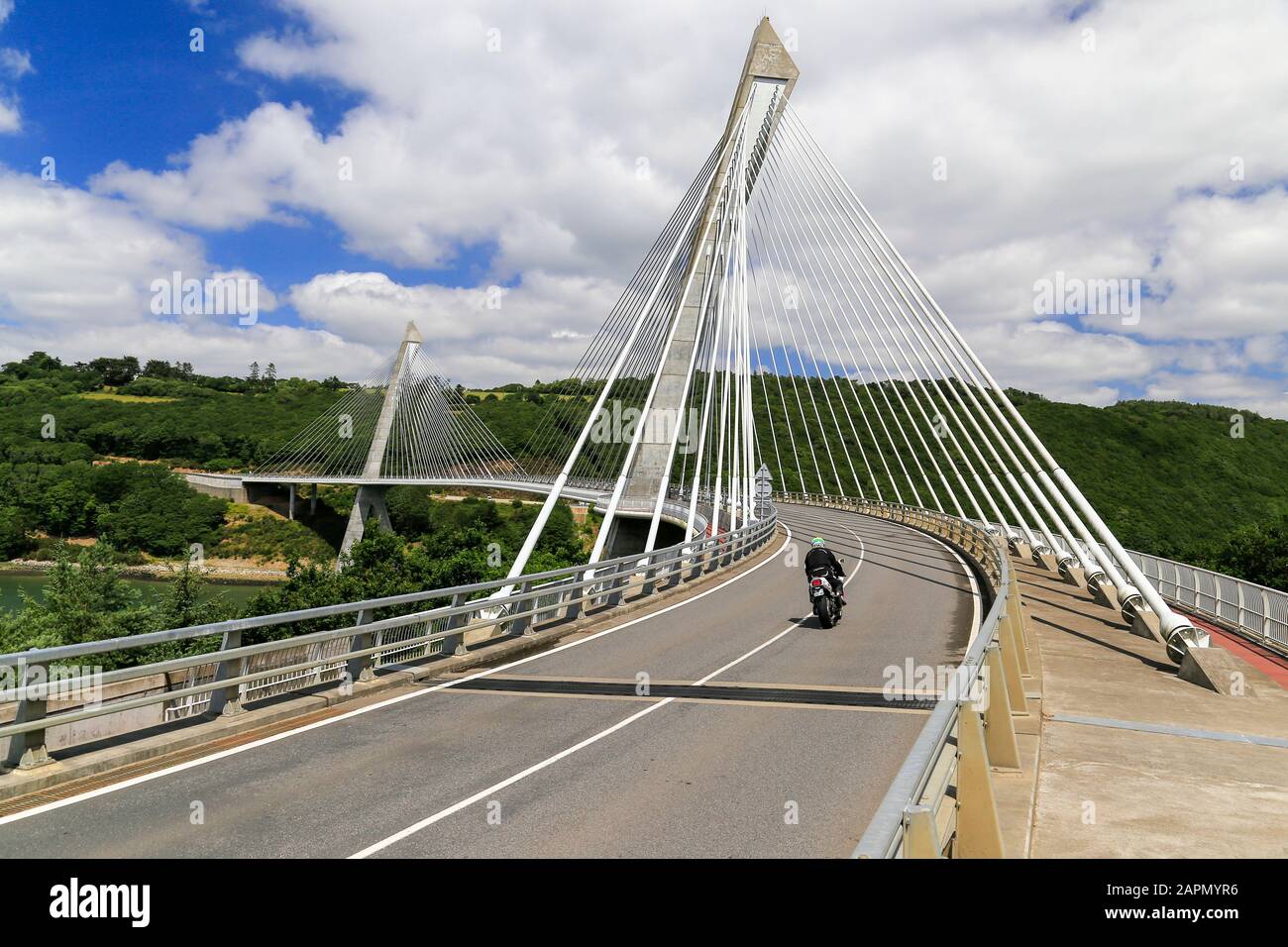 Solo motorcycle crossing modern, curved, suspension bridge in France. Stock Photo