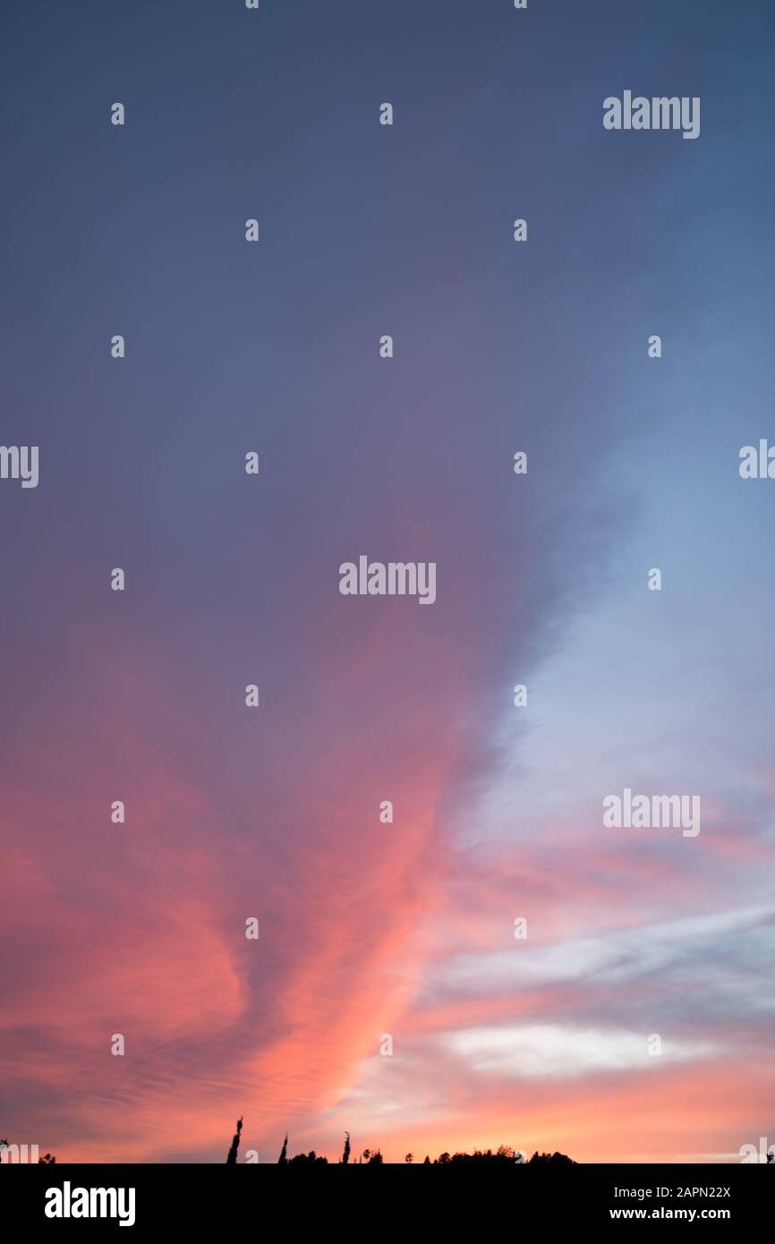 Vertical shot of pink clouds in a clear blue sky with scenery of ...