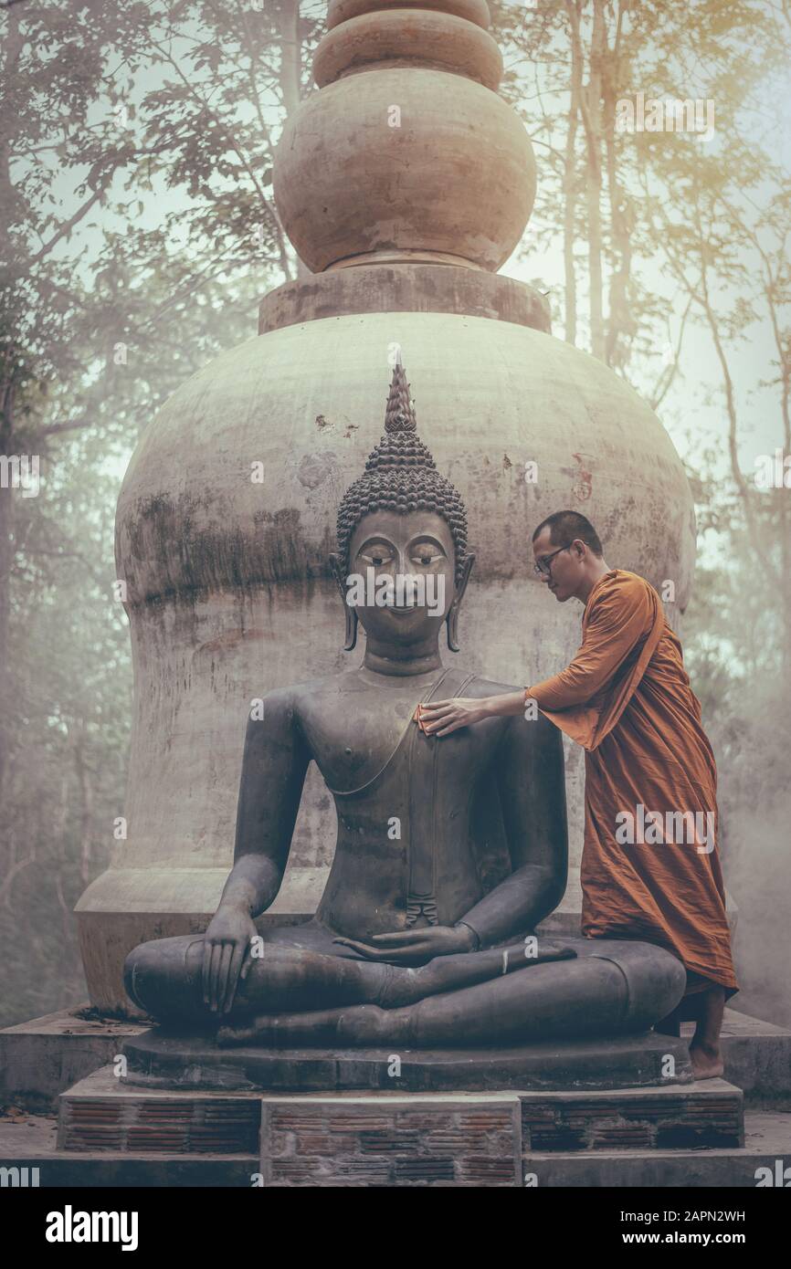 Monk scrubbing buddha statue at temple in Thailand Stock Photo