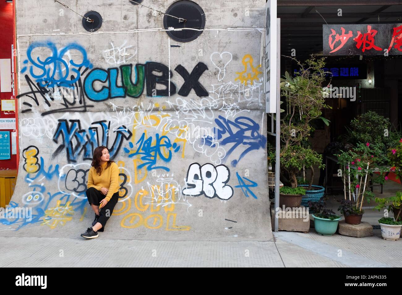 A young Chinese woman poses for a photo against a wall of graffiti at