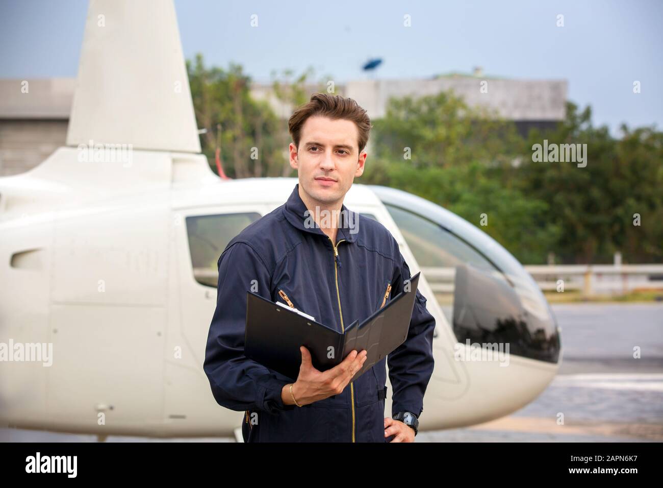 Commercial man pilot in technician suit standing in front of helicopter after check and maintenance engine Stock Photo