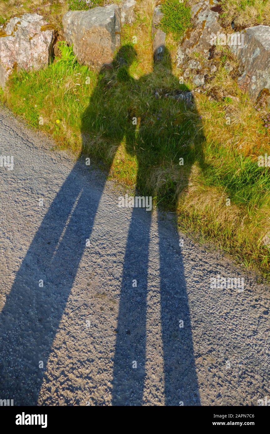 Ein Mann und eine Frau werfen einen langen Schatten auf Straße und Wiese Stock Photo