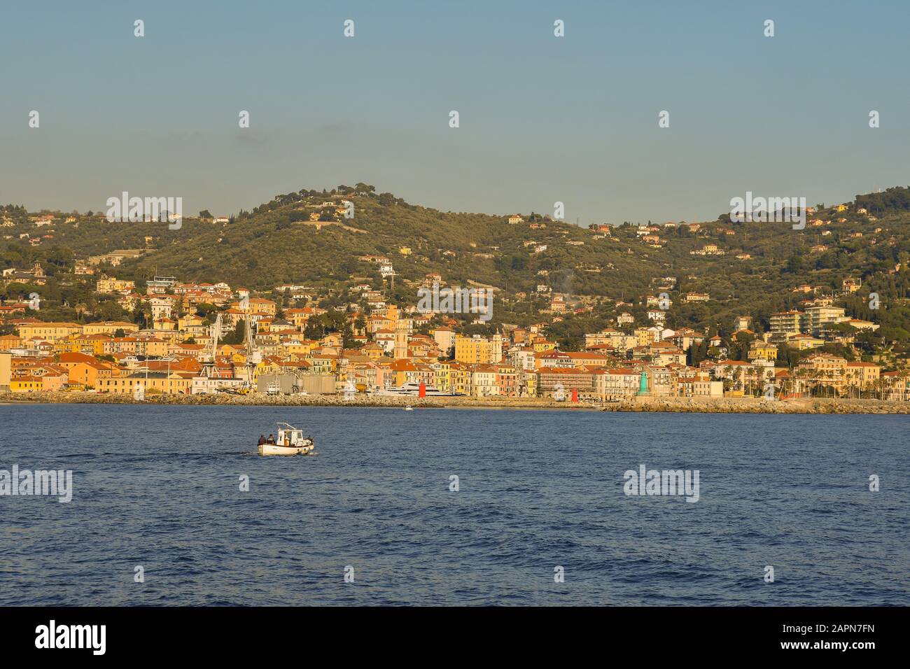 Scenic view from the sea of the coastal city of Oneglia in the Riviera of Flowers with a passing fishing boat in a sunny day, Imperia, Liguria, Italy Stock Photo