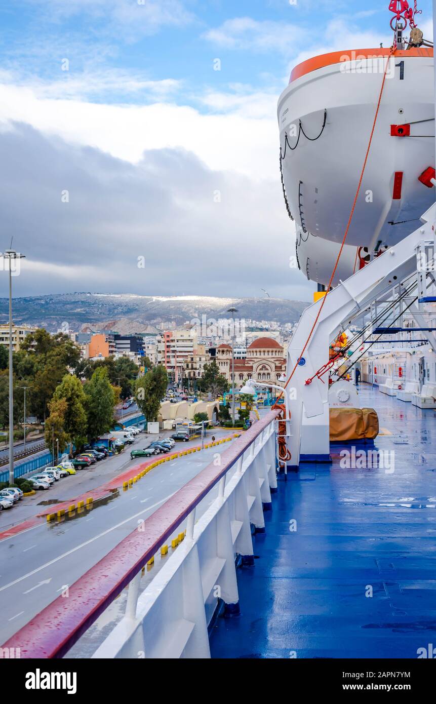 Open deck corridor of a ferry boat with rescue boats and the port of Piraeus in background. Stock Photo