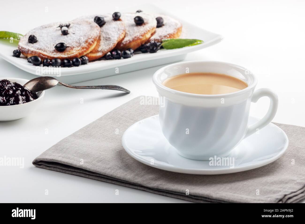 A Cup of coffee with milk and a plate with a pancakes is on the table. Stock Photo
