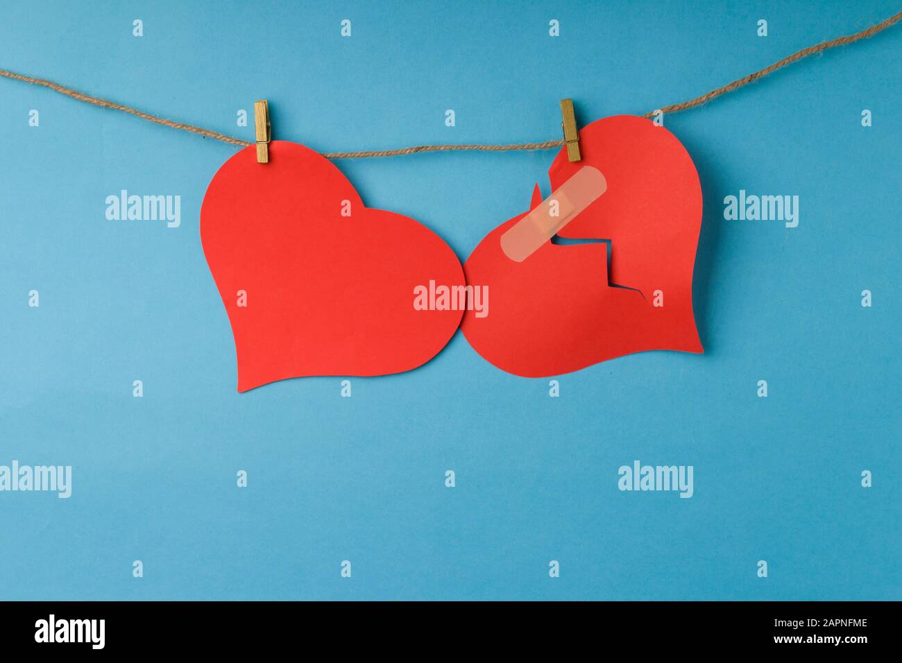 Red broken heart and whole heart hanging on rope. Stock Photo