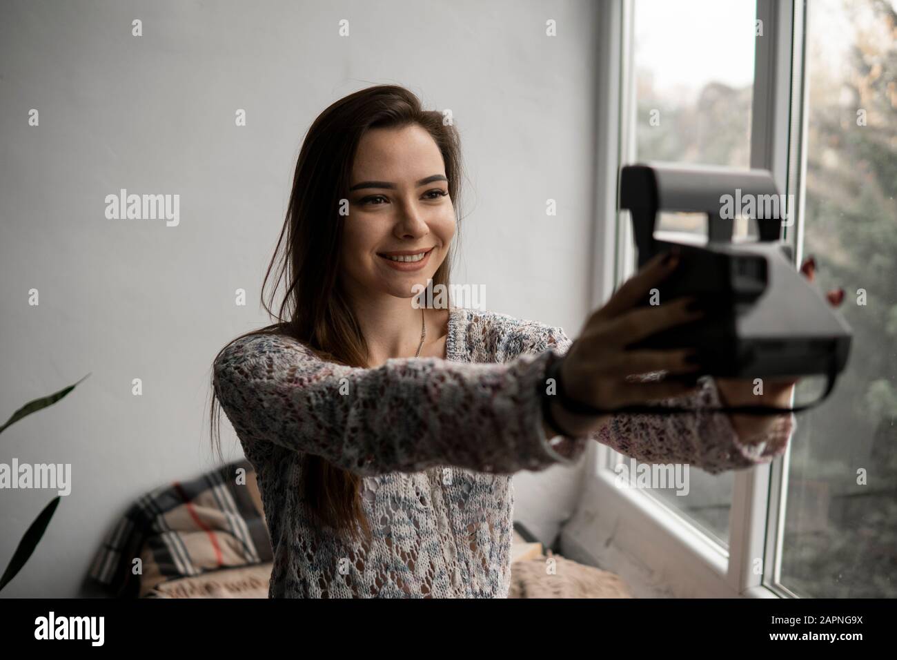 Smiling young brunette woman takes photographs selfie portrait with old photo camera. Stock Photo