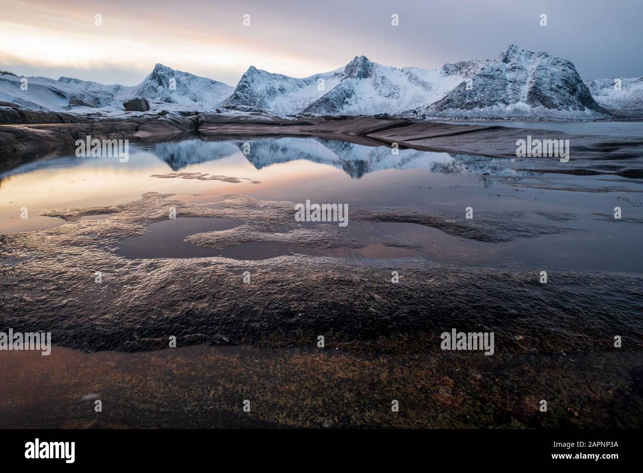 View over rockpool to snowy mountain range in evening light with beautiful reflections, Cape Tungeneset, Ersfjord, Senja, Norway Stock Photo
