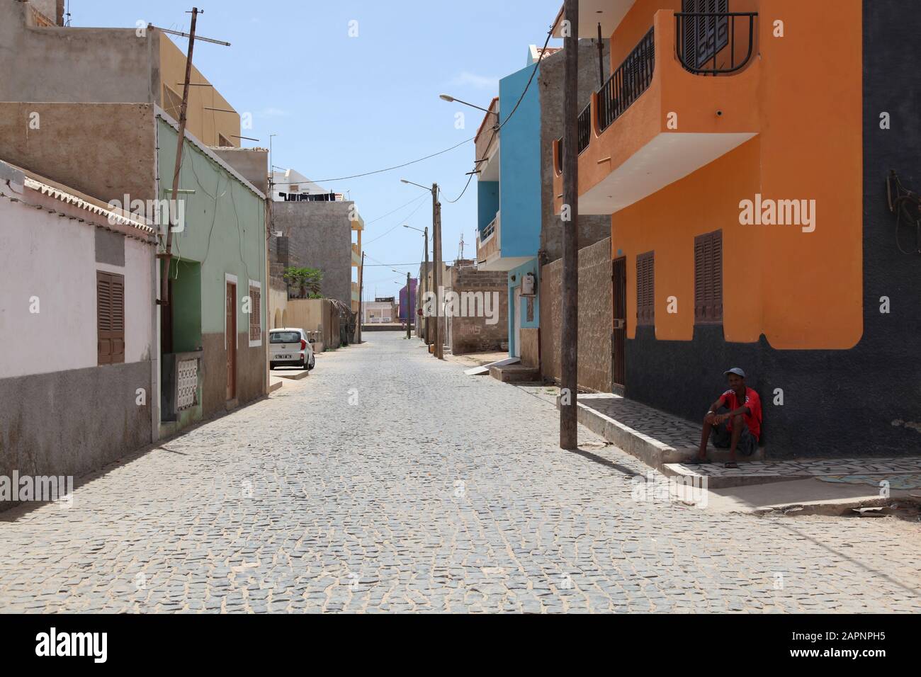 A deserted main street at siesta time with local man resting in the shade by side of the road in Santa Maria, Sal, Cape Verde, Africa Stock Photo
