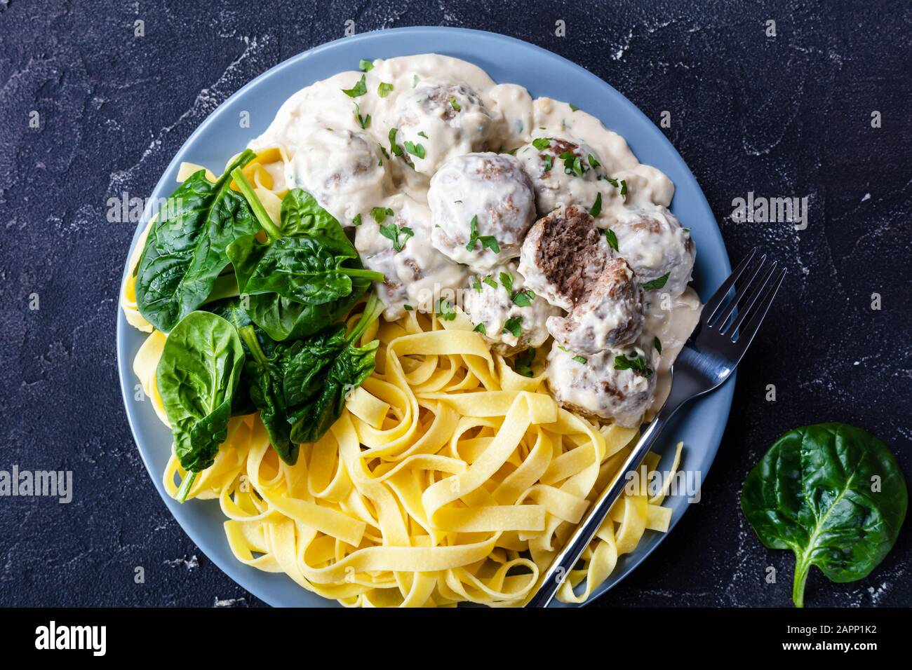 classic Swedish meatballs served with egg noodle and fresh spinach leaves on a plate with silver fork on a concrete kitchen table, horizontal view fro Stock Photo
