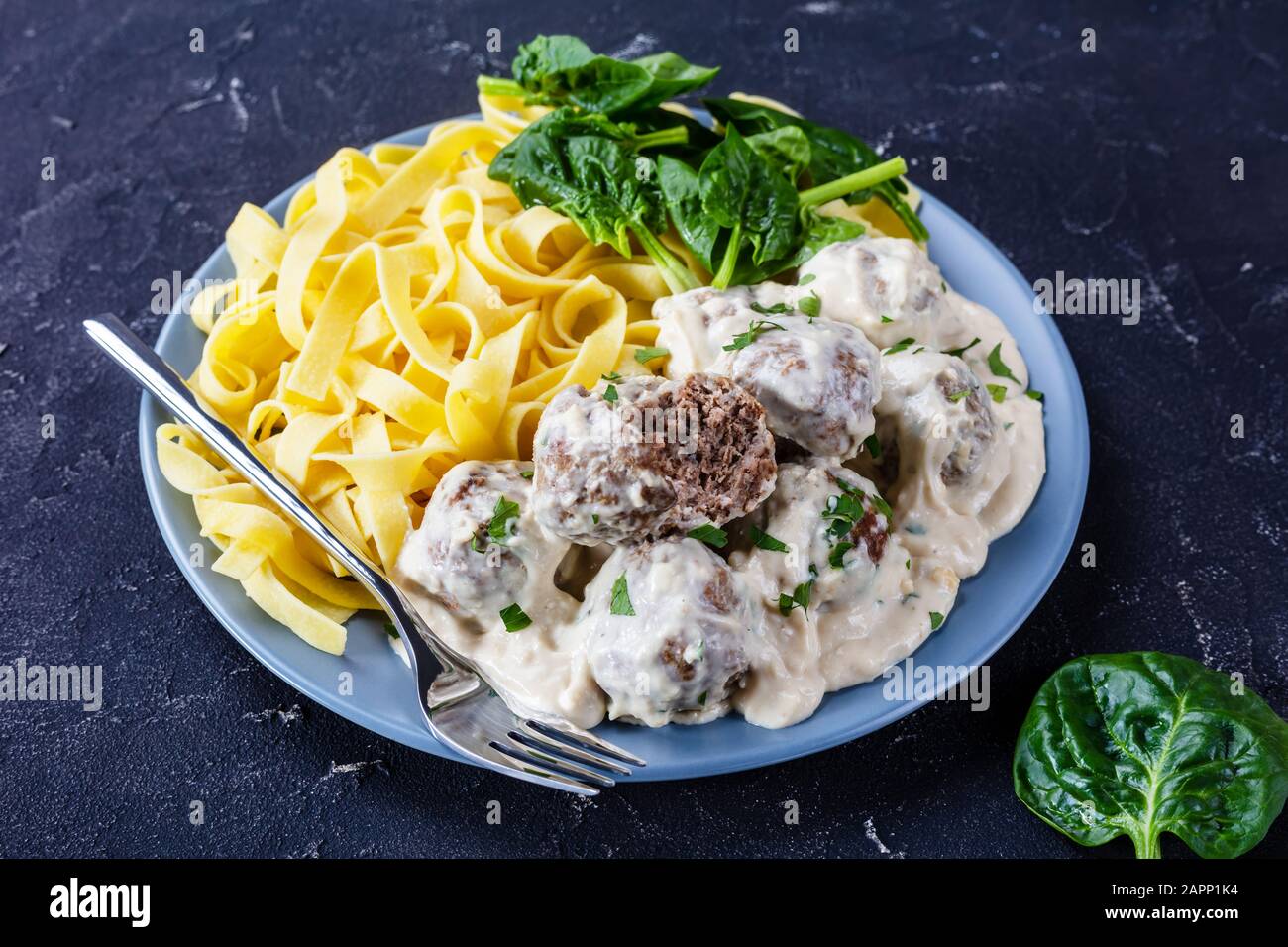 classic Swedish meatballs served with egg noodle and fresh spinach leaves on a plate on a concrete kitchen table, view from above, close-up Stock Photo