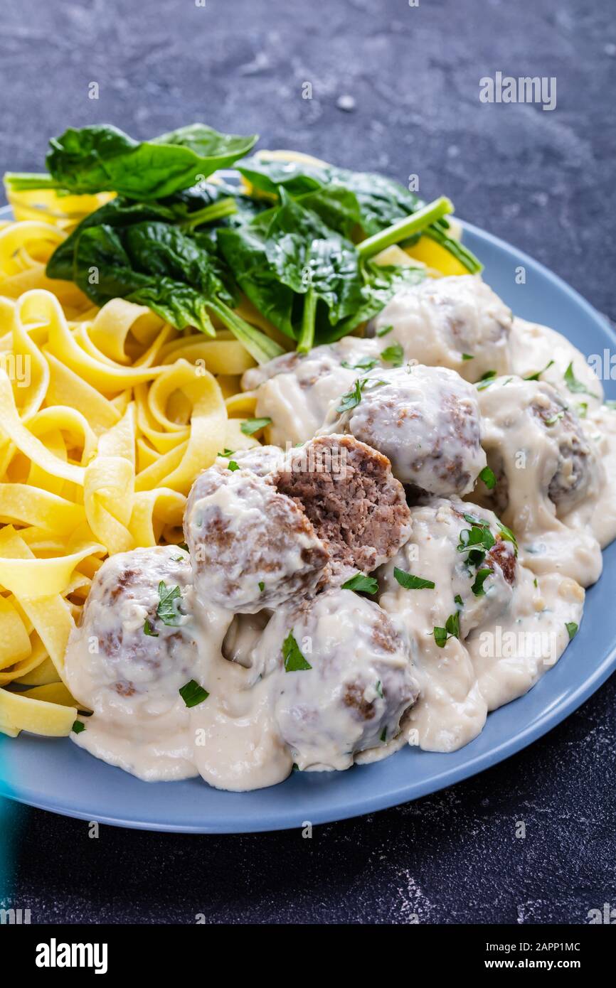 classic Swedish meatballs served with egg noodle and fresh spinach leaves on a plate on a concrete kitchen table, vertical view from above, close-up Stock Photo