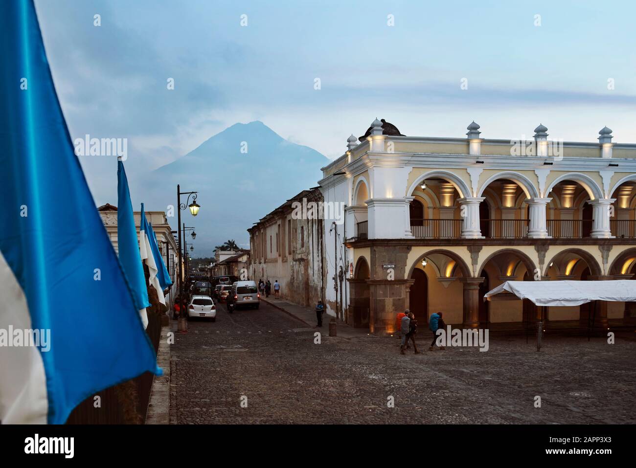 Street scene of Avenida Sur with Volcan de Agua in the background. Backpackers crossing Plaza Mayor (Parque Central), Antigua, Guatemala Stock Photo
