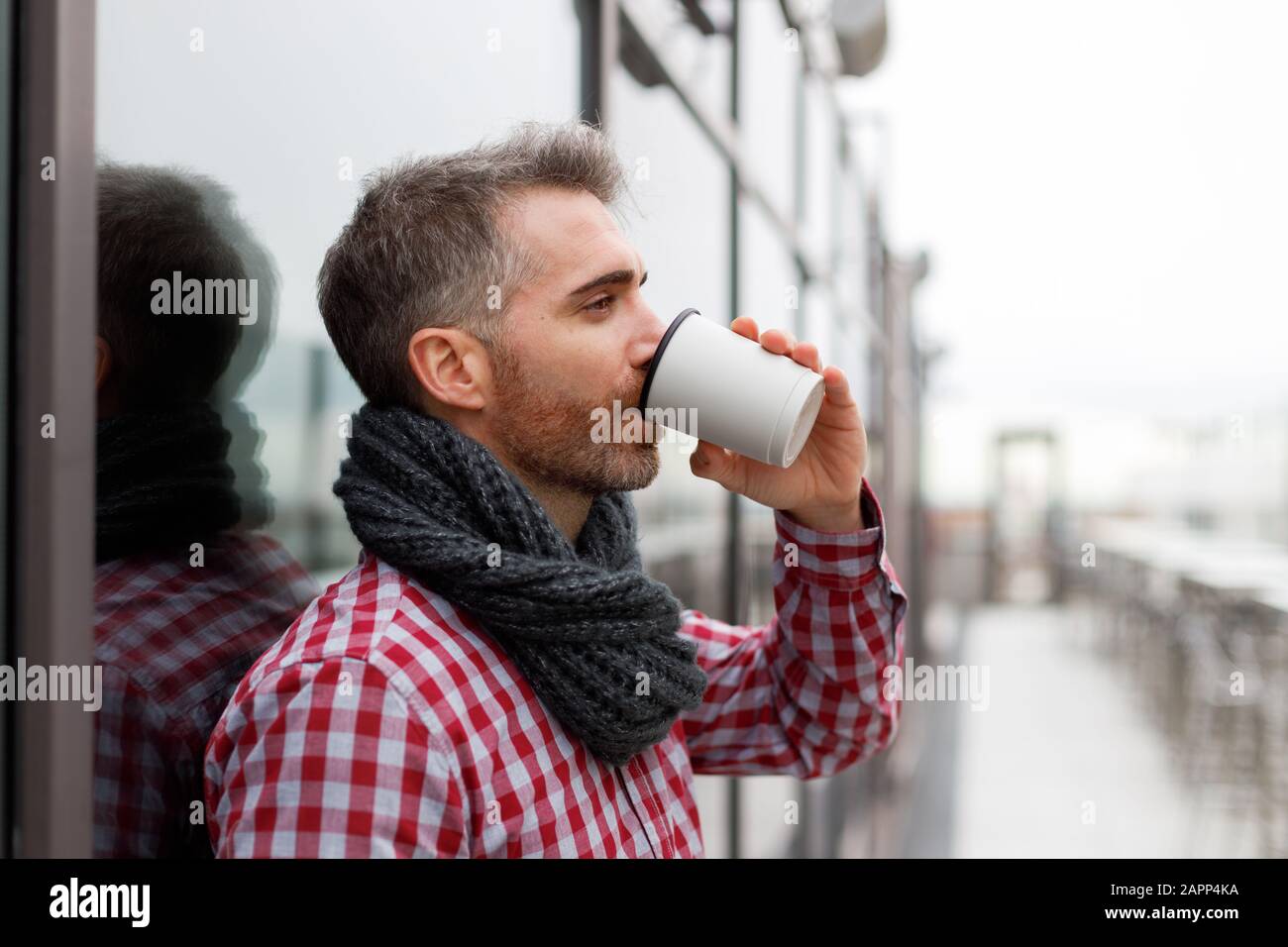 Young man leaning against a wall drinking from a reusable cup Stock Photo