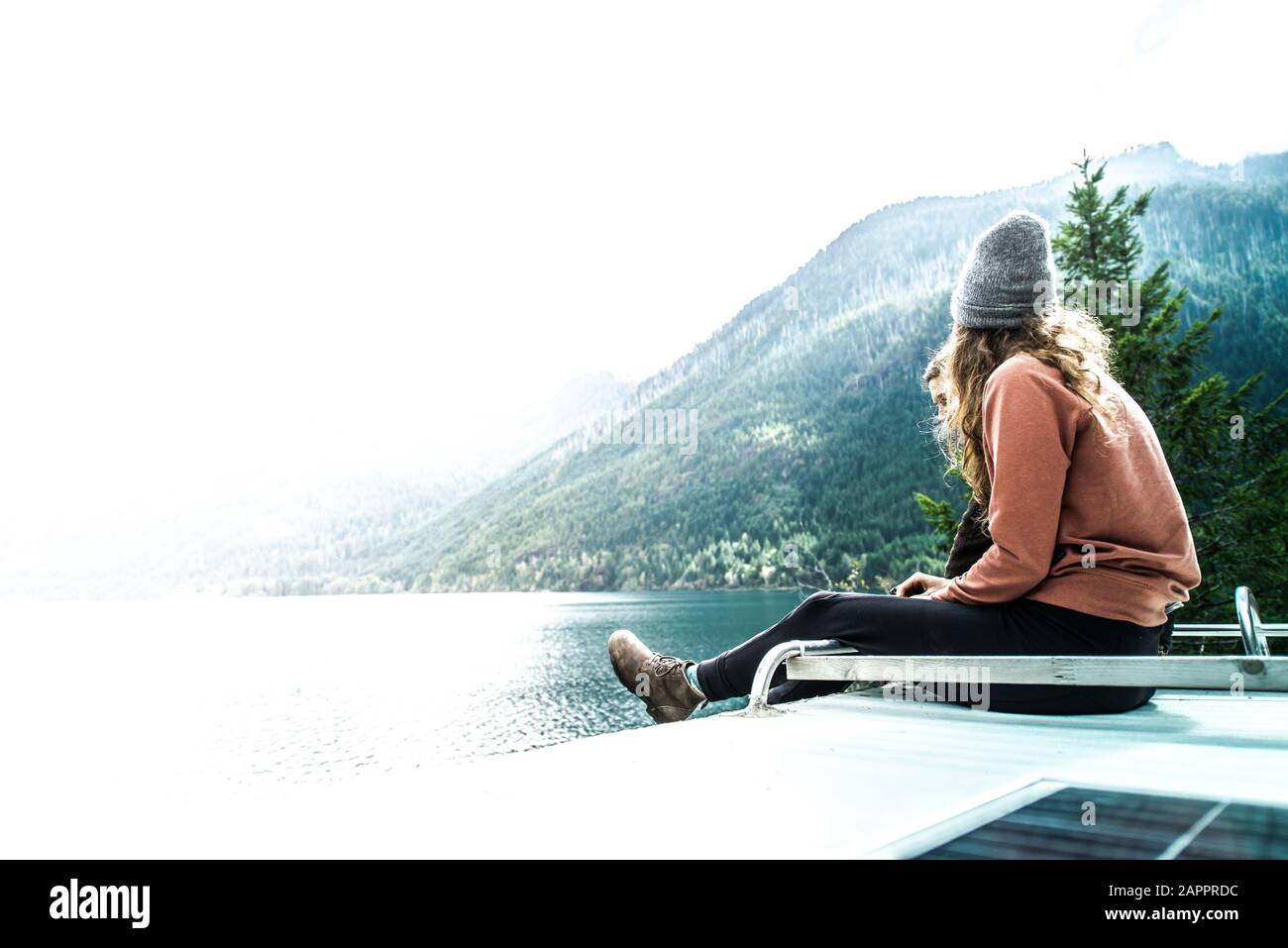 Woman seated on top of campervan overlooking the lake, Cathedral Grove, British Columbia, Canada Stock Photo