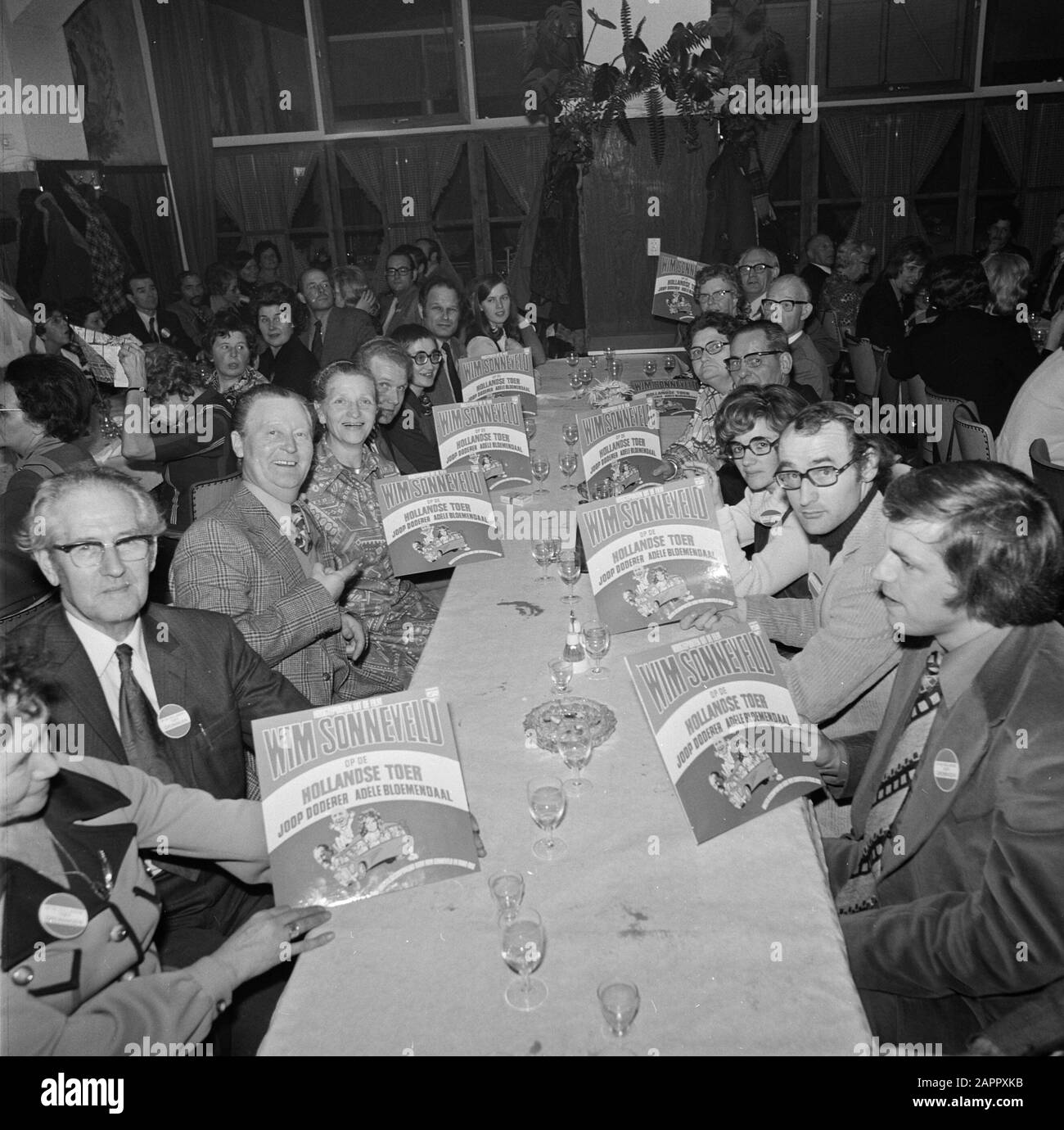 The album with material from the film On the Dutch tour  Group of people at the table with the gramophone record Date: 19 December 1973 Location: Noord-Holland, Volendam Keywords: films, gramophone records, soundtracks Settings name: Newsblad van het Noorden Stock Photo