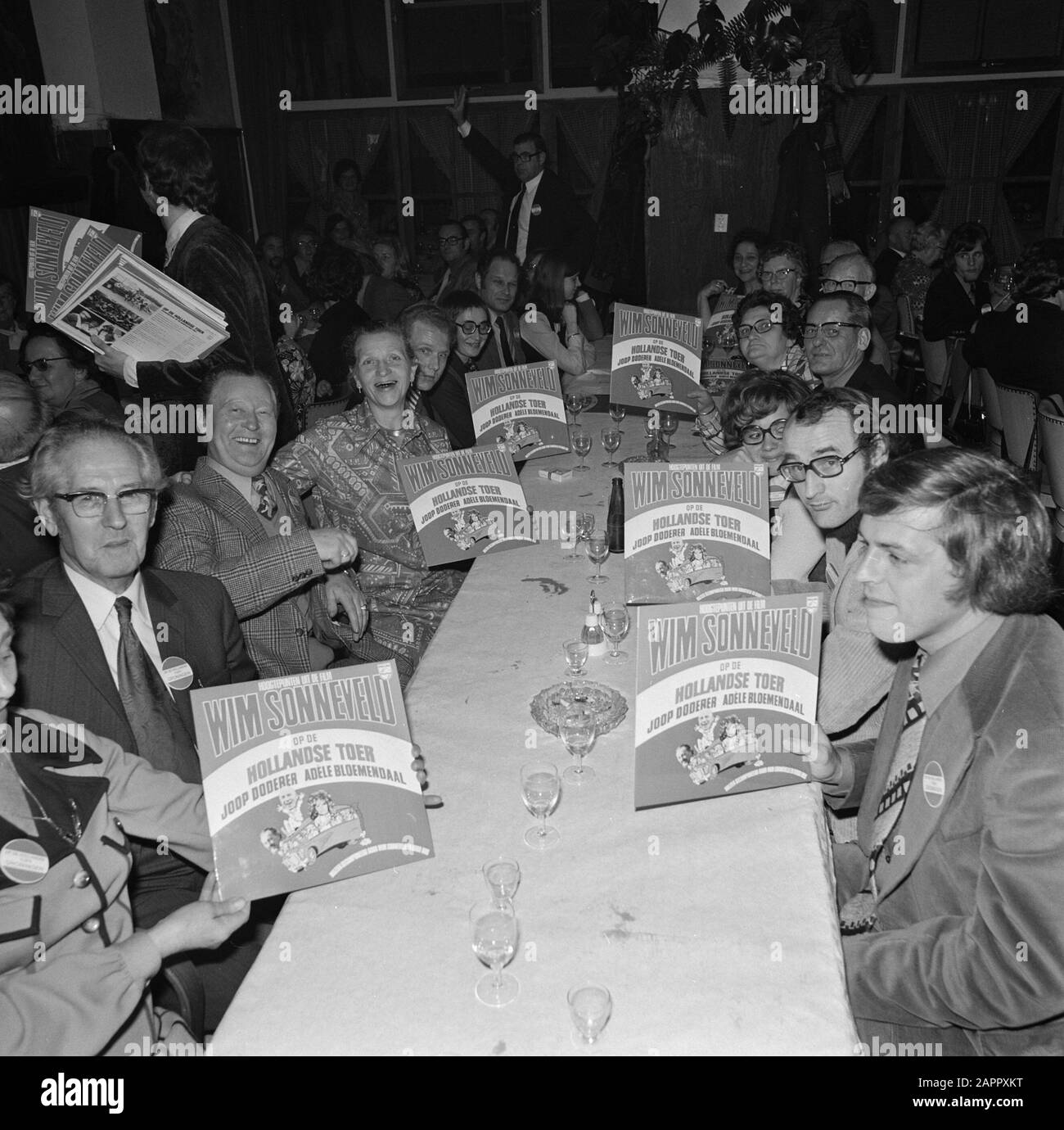 The album with material from the film On the Dutch tour  Group of people at the table with the gramophone record Date: 19 December 1973 Location: Noord-Holland, Volendam Keywords: films, gramophone records, soundtracks Settings name: Newsblad van het Noorden Stock Photo