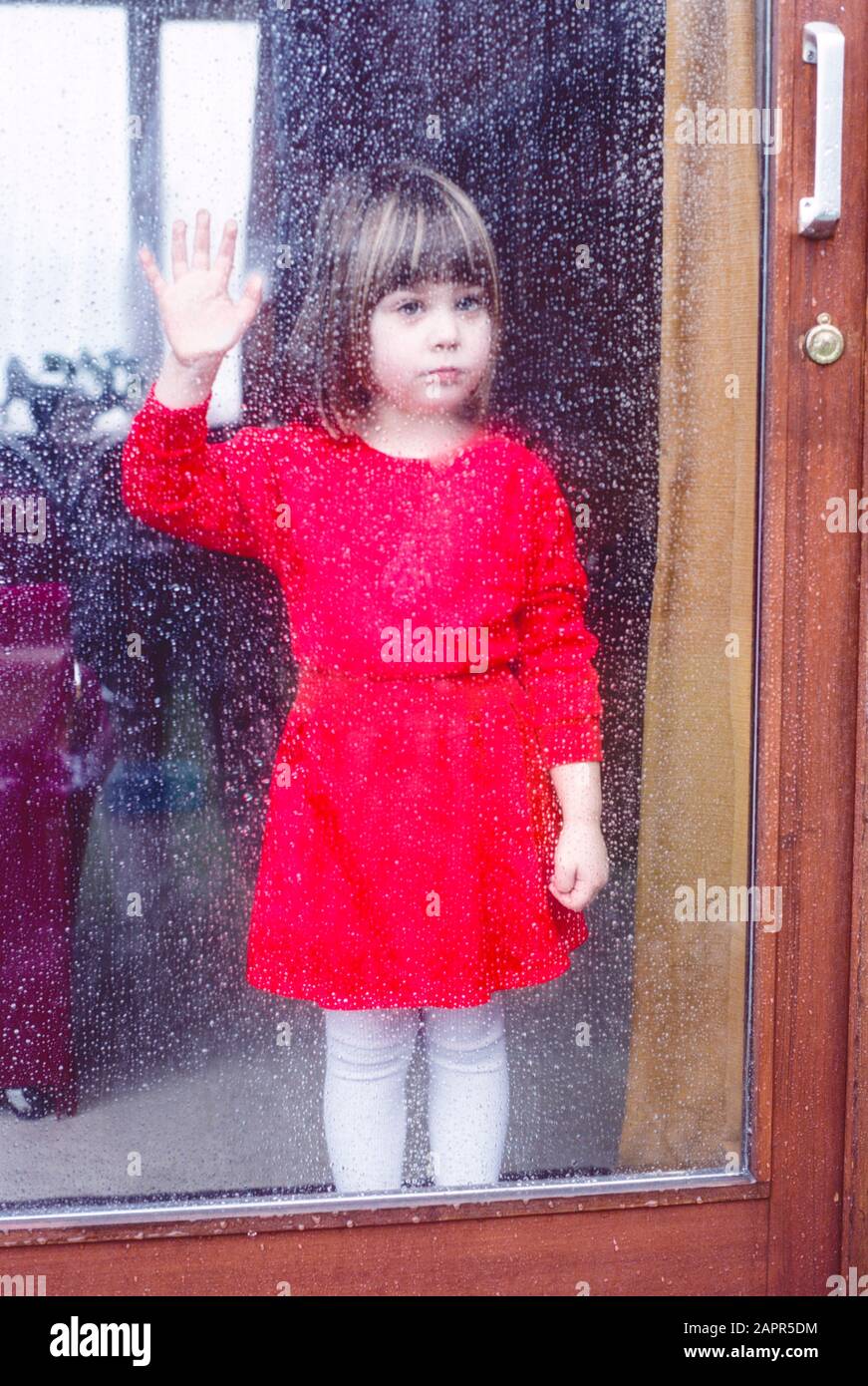little girl stuck indoors looking out through glass patio door covered