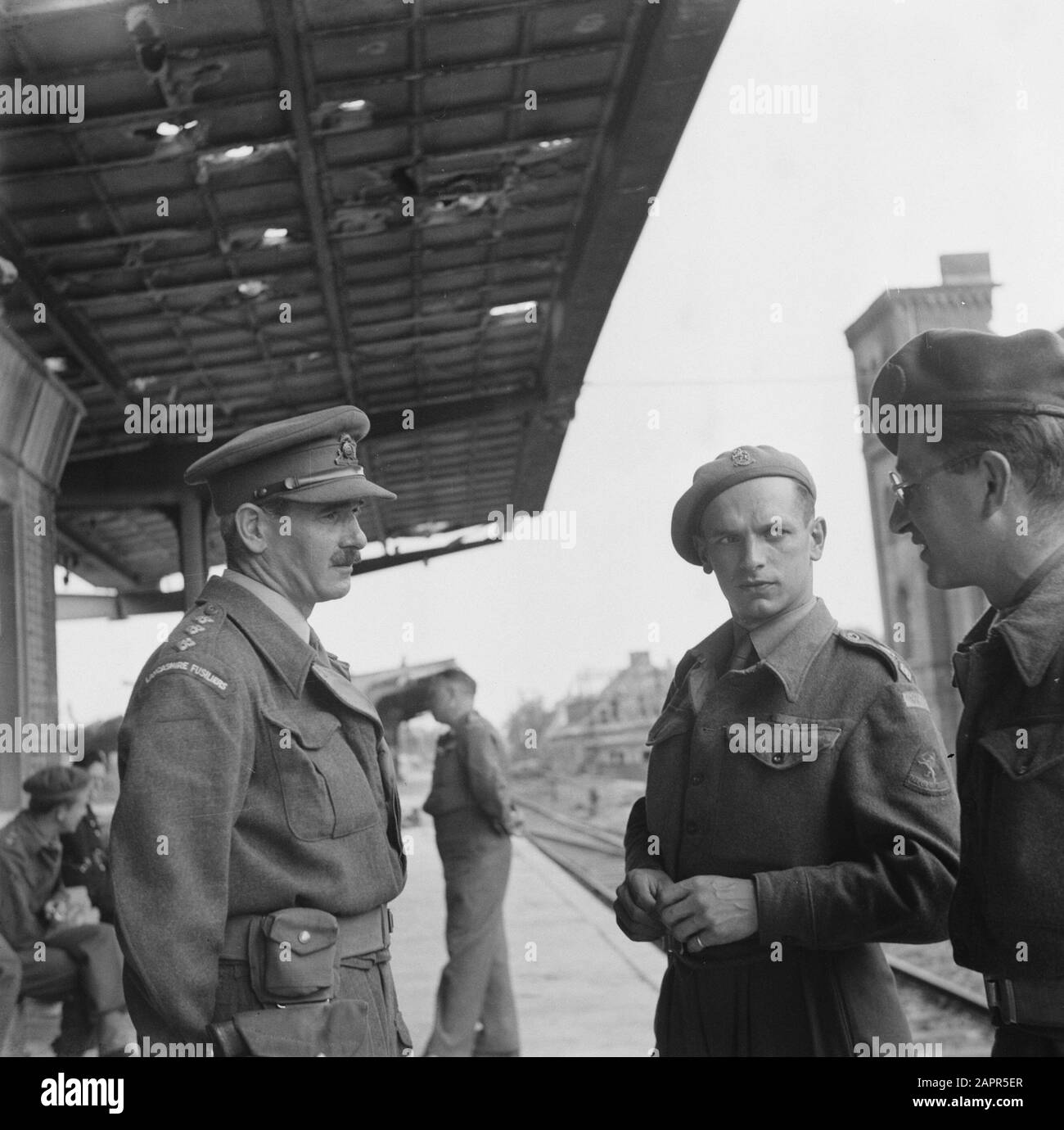 Repatriation Camp Rheine (Germany)  [Soldiers talking at a railway station. A captain of the Lancashire Fusiliers on the left. In the middle a man in uniform with English markings but a Dutch sleeve emblem (Je Maintiendrai) Annotation: Repatriëringskamp. Date: 1945 Location: Germany, Rheine Keywords: repatriation, World War II Stock Photo