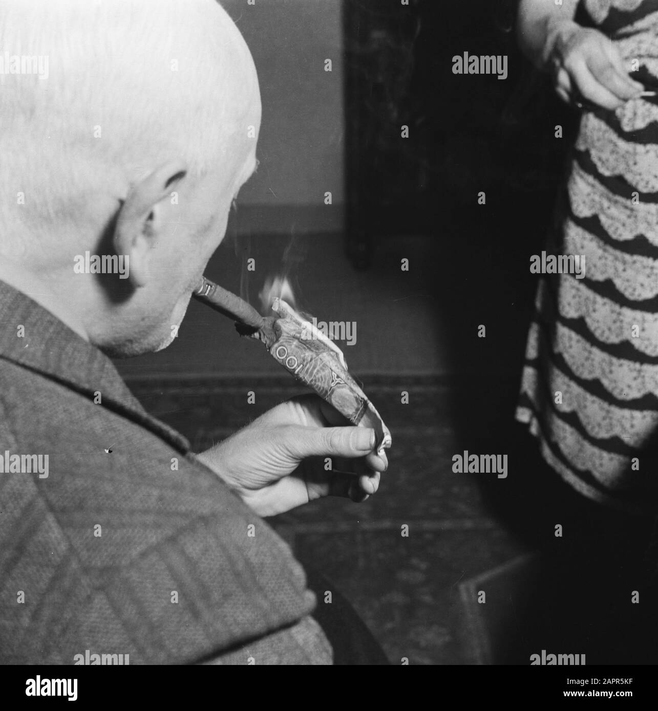 Finance: Money Purge  Man lights cigar with become worthless 100 guilder banknote Date: July 1945 Keywords: banknotes, cash purges, cigars, World War II Stock Photo