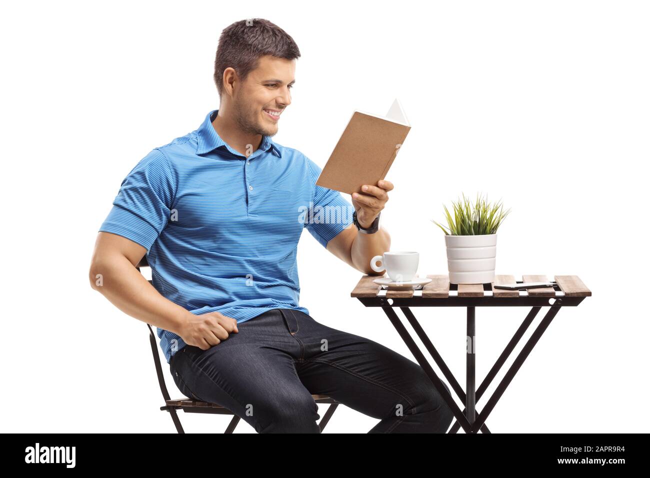 Guy sitting at a coffee table and reading a book isolated on white background Stock Photo