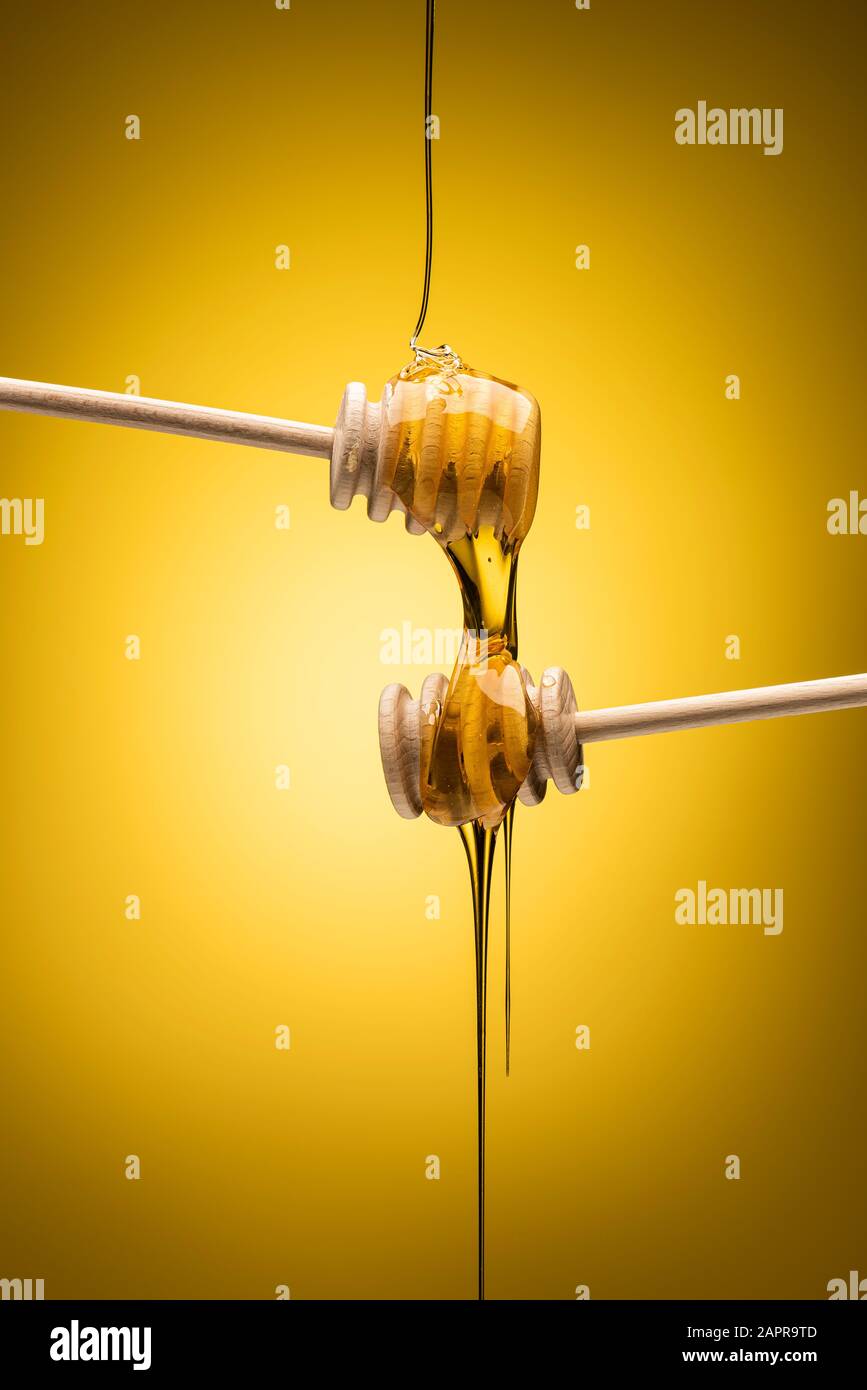Honey dripping from wooden dipper on yellow background Stock Photo
