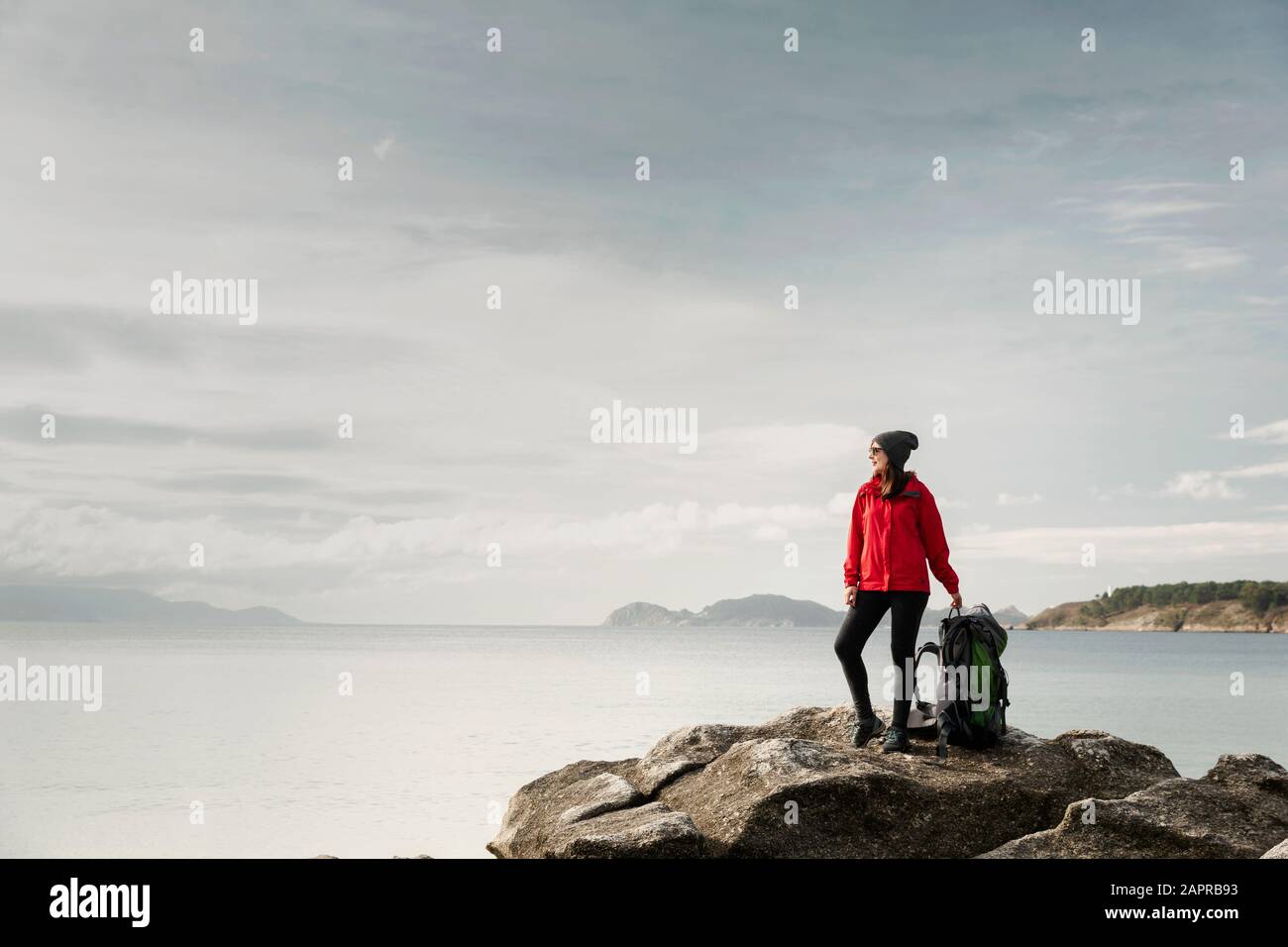 Woman with backoack enjoying the morning view of the coast Stock Photo