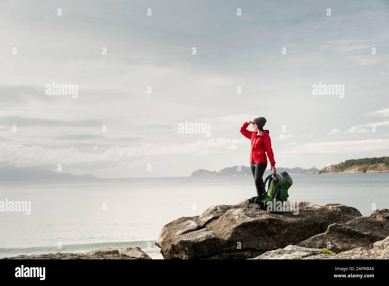 Woman with backoack enjoying the morning view of the coast Stock Photo