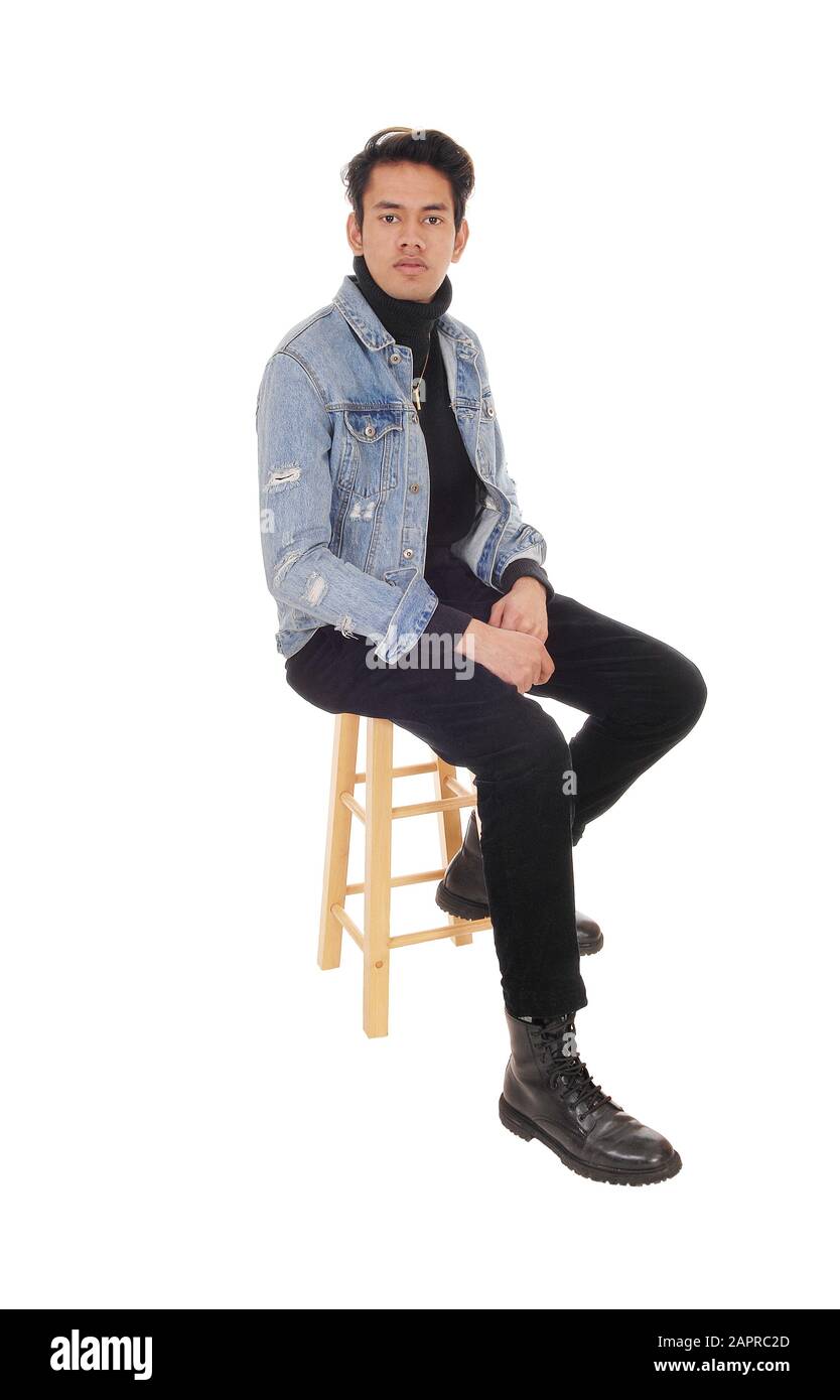 A young handsome man sitting in a jeans jacket and black pants on a chair, resting, isolated for white background Stock Photo