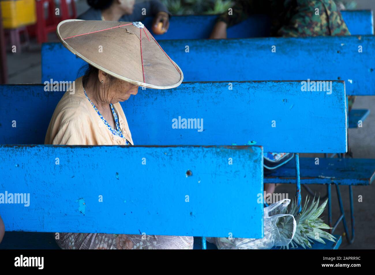 Senior Burmese woman with asian conical hat, sitted on blue bench Stock Photo