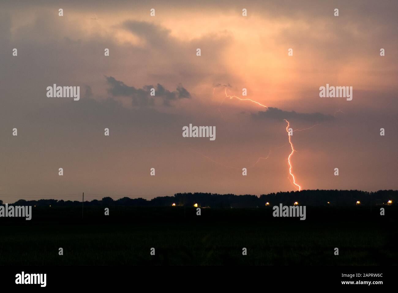 Red colored lightning bolt strikes from a distant thunderstorm Stock Photo