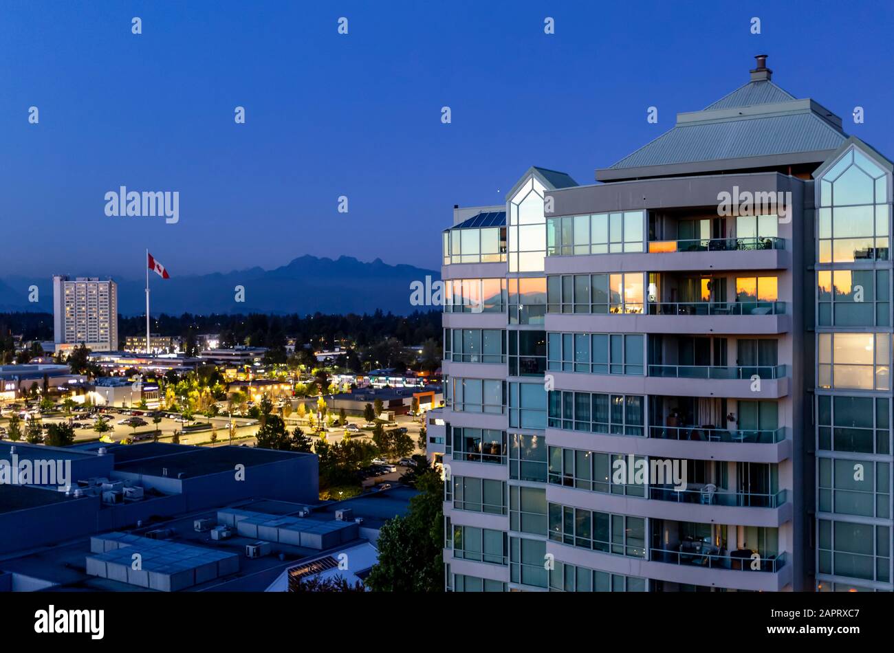 Residential building at twilight with a Canada Flag and mountains in the distance; Surrey, British Columbia, Canada Stock Photo