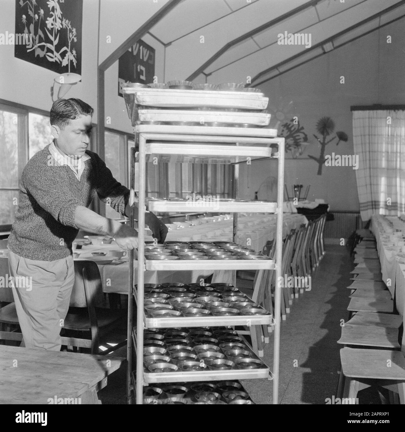 Israel 1964-1965: Gal'ed, since evening  A man serving a particular dish in connection with celebrating in the community space of Seideravond (sederdiner). Annotation: Gal'ed (also called Even Yitzhak) is a kibbutz in northern Israel, located in the plain of Manasseh. In 2006 it had a population of 405. Seder Evening (also called Seideravond) is an evening at the beginning of the Passover festival, where Jews from the Haggada read (booklet about the story of Jewish slavery in Egypt and the exodus from Egypt), drink 4 glasses of wine (or grape juice) and a festive sedermeal. Seder literally mea Stock Photo