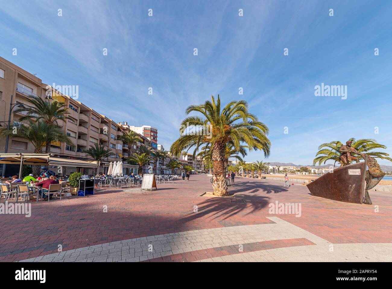 Seafront promenade in Puerto de Mazarron, Murcia, Costa Calida, Spain, on the Mediterranean coast. People in al fresco bar, cafe. Fisherman sculpture Stock Photo