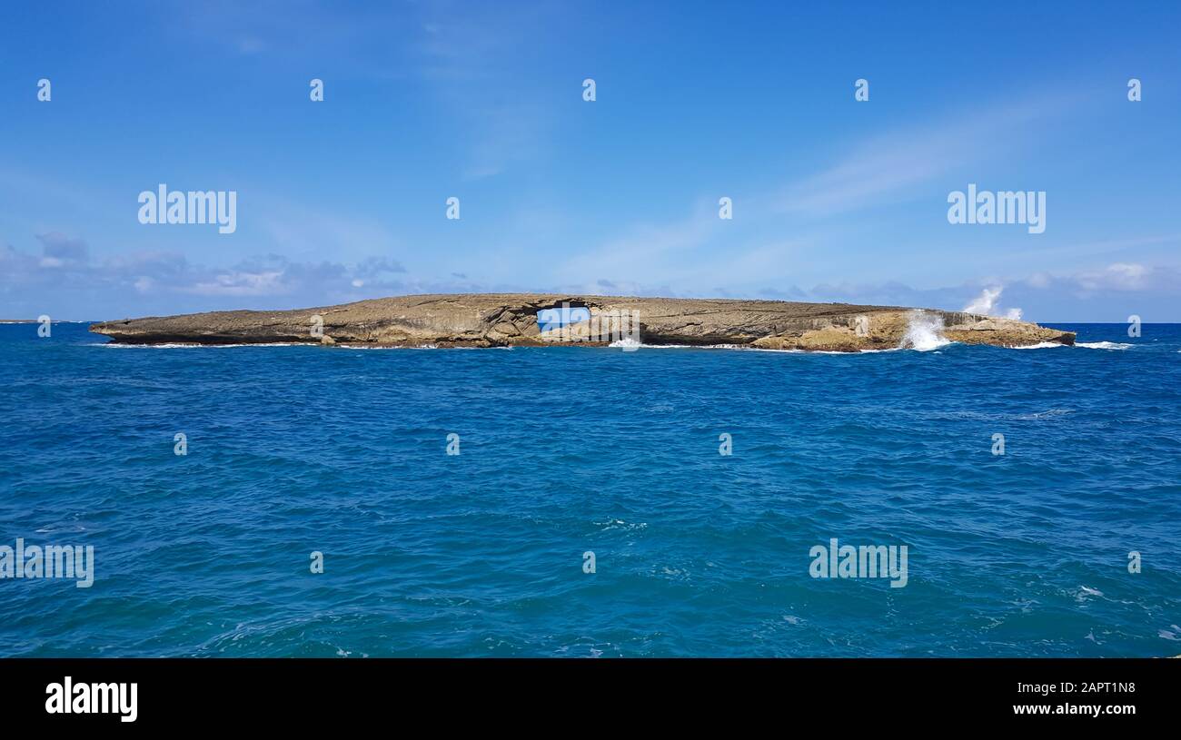 A wave breaks on small island off the coast of Oahu, Hawaii shoots water high into the air. Stock Photo